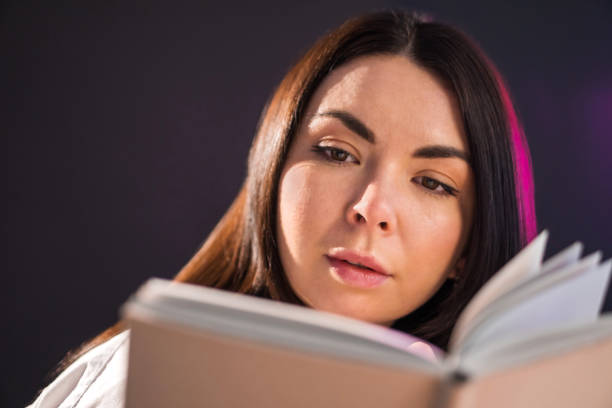 istock Young brunette girl is reading exciting book over black background. 1296577286