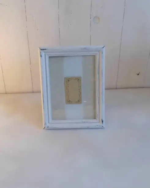 White chalk paint distressed picture frame on white back ground.  Inside frame is beige and white artwork.