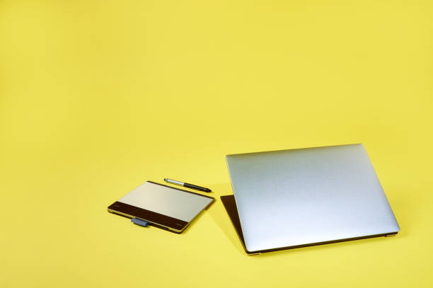 istock Flay lay composition of a silver grey laptop lying near a graphics tablet isolated on a yellow background. Copy space 1296582636