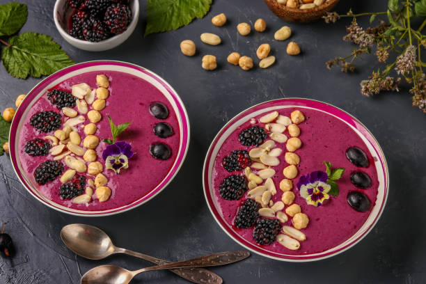 istock Healthy breakfast smoothie bowl with blackberries, gooseberries, peanuts, hazelnuts, decorated with flowers on a dark background, horizontal photo 1296584174
