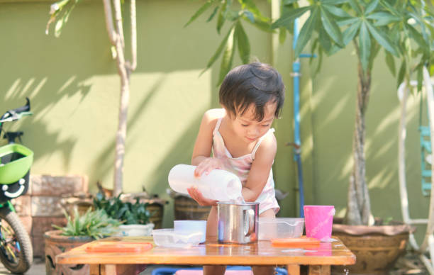 アジアの幼児の女の子は、カップに水を注ぐ楽しみを持って, 湿った注ぐモンテッソーリ就学前の実生活活動, 細かい運動能力開発, 安全に滞在安全滞在 楽しいコンセプトを持っています - fine motor skills ストックフォトと画像