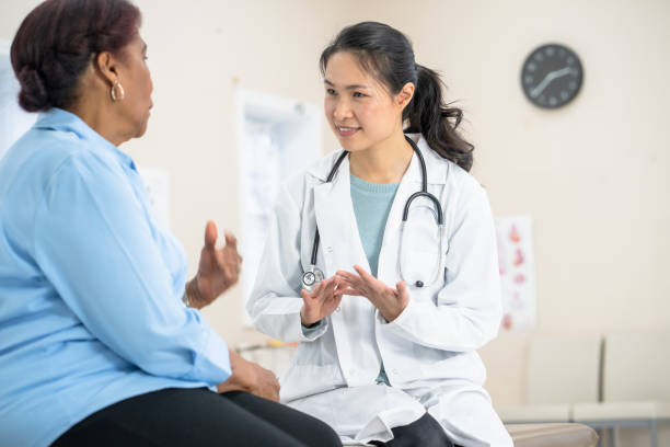 Female Asian doctor with patient A beautiful young female doctor wearing a white lab coat is at her medical clinic and with a patient. ovarian cancer stock pictures, royalty-free photos & images