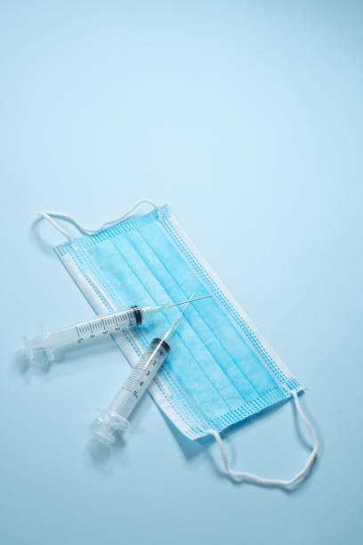 istock MASK AND SYRINGES ON BLUE BACKGROUND 1296608353