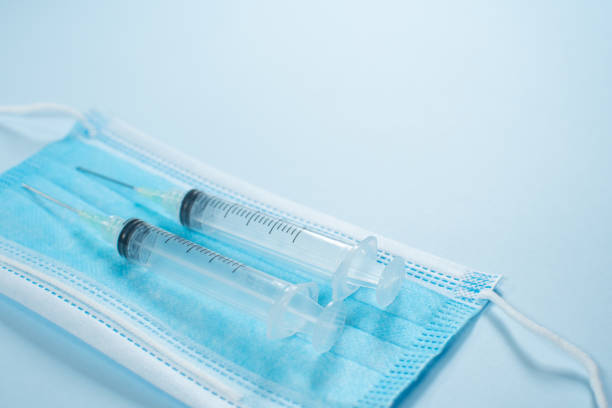 istock MASK AND SYRINGES ON BLUE BACKGROUND 1296608720
