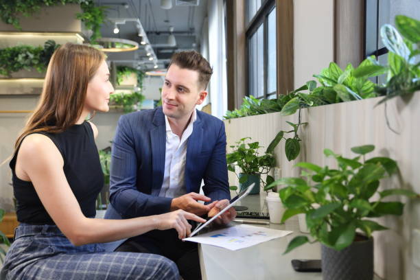 Caucasian businessman is showing his coworker new strategic planning for next year using digital tablet while working in green eco friendly modern working space surrounded by air purifying house plant empresario caucásico está mostrando a su compañero de trabajo nueva planificación estratégica para el próximo año utilizando tabletas digitales mientras trabaja en un espacio de trabajo moderno ecológico rodeado de planta de purificación de aire