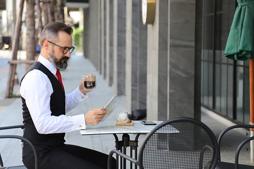 Caucasian middle age man in formal wear using digital tablet to order food from outdoor café and restaurant at the European square for contactless and payment system