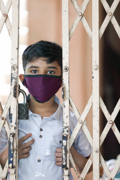 istock young Indian boy wearing protective mask and watching out at home 1296628670