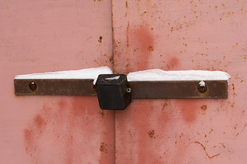 padlock on an old iron gate with peeling paint and traces of rust. there is snow on the lock and metal plates