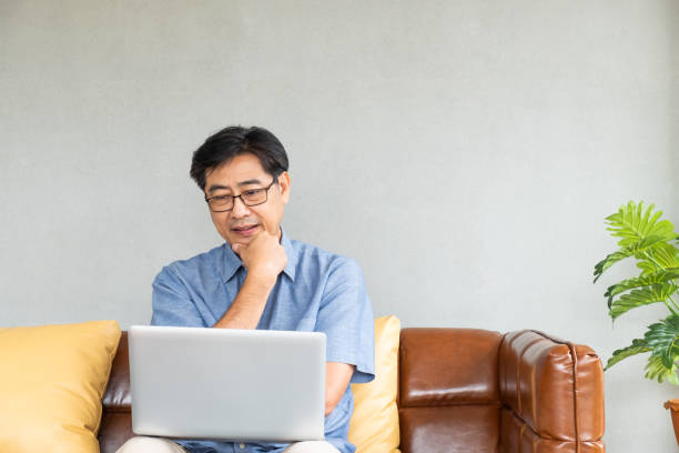 enfoque selectivo en los hombres de asia vieja se sientan en el sofá, teniendo dificultad y problema con internet y computadora portátil.  ancianos que aprenden nuevas tecnologías o problemas de salud visual. - pain human eye senior adult men fotografías e imágenes de stock