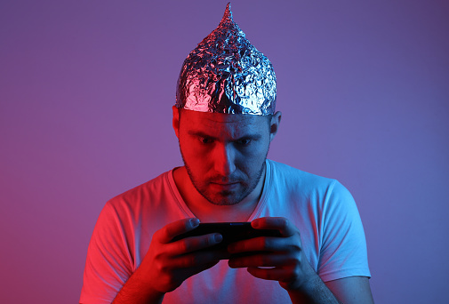 Hombre barbudo loco en sombrero de lámina juega con el teléfono inteligente en la luz de neón azul rojo. photo