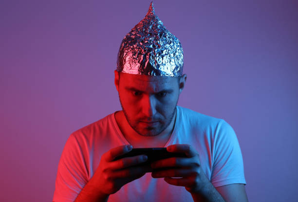 Crazy Bearded Man in Foil Hat Plays with Smartphone in Red Blue Neon Light. Crazy Bearded Man in Foil Hat Plays with Smartphone in Red Blue Neon Light. conspiracy stock pictures, royalty-free photos & images