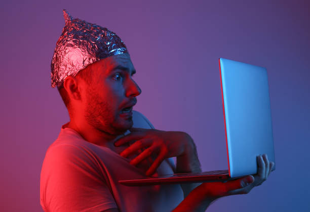 Crazy Bearded Man in a foil hat with a laptop in red blue neon light. Conspiracy Crazy Bearded Man in a foil hat with a laptop in red blue neon light. Conspiracy tin foil hat stock pictures, royalty-free photos & images