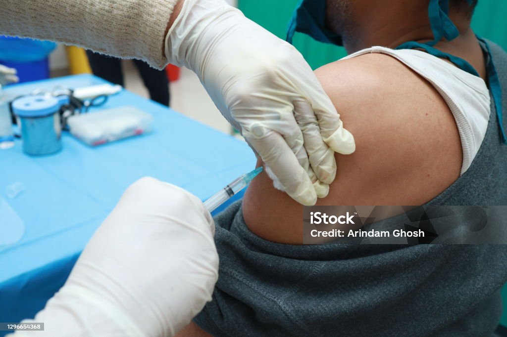 a close up photo of an intra muscular covid vaccine being given in arm of a patient by a doctor with gloved hand with selective focus on arm. India Stock Photo