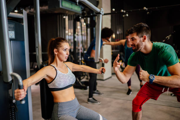 istock Woman working out on exercise machine with instructor at gym 1296660192