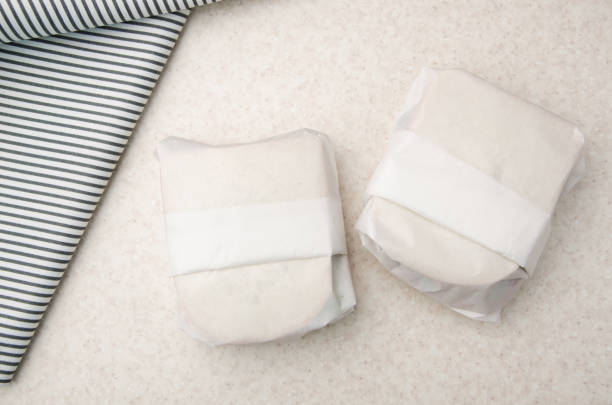 flat lay view at two sandwiches wrapped in parchment paper on kitchen table - papel de pão imagens e fotografias de stock