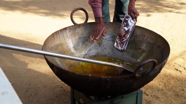 Man poring out fragrant hot spices in iron cauldron to prepare delicious vegetable. stock photo