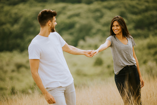 Happy young couple in love walking through grass field on a summer day