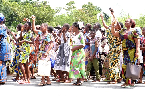 Kpalimé, Togo - November 24, 2019: Welldressed catholics walk with their pastor on the public road. They wear colorful african textiles dresses on their way to church in Kpalimé, Togo, West Africa. They sing and pray during their excursion.