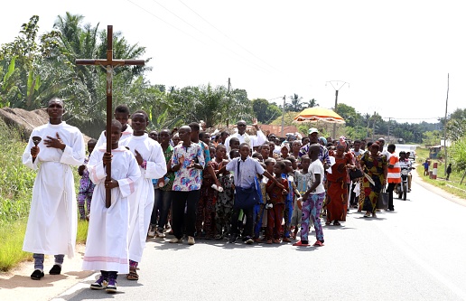 Kpalimé, Togo - November 24, 2019: Welldressed catholics walk with their pastor on the public road. They wear colorful african textiles dresses on their way to church in Kpalimé, Togo, West Africa. They sing and pray during their excursion.