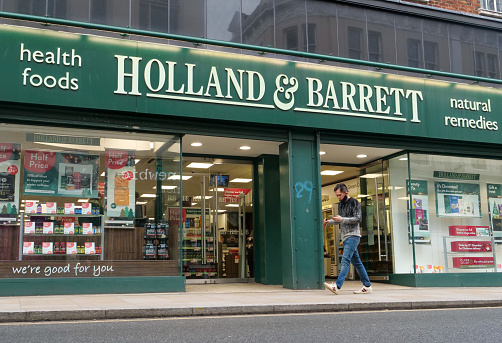 London,UK- December 26, 2020:The retail store of Holland&Barrett in London. Holland & Barrett (H&B) is a chain of health food shops with over 1,300 stores in 16 countries, Pedestrian crossing on front of the entrance.