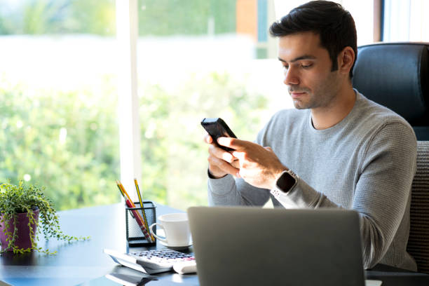 istock Young Businessman at home working on laptop. Man holding Mobile phone and using his mobile phone. Work from home. 1296669898