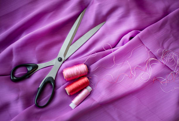 Pink textile silk background with spools of thread and with scissors. Template for text message announcement. Themes of needlework of tailoring of making clothes and linen.