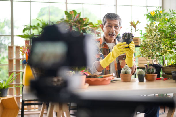 istock A senior man entrepreneur working with camera presents houseplants during online live stream at home, selling online concept 1296671134
