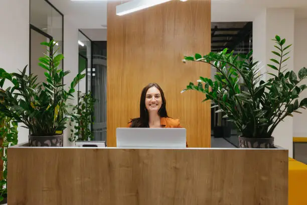 Portrait of smiling female lobby receptionist sitting at front desk.