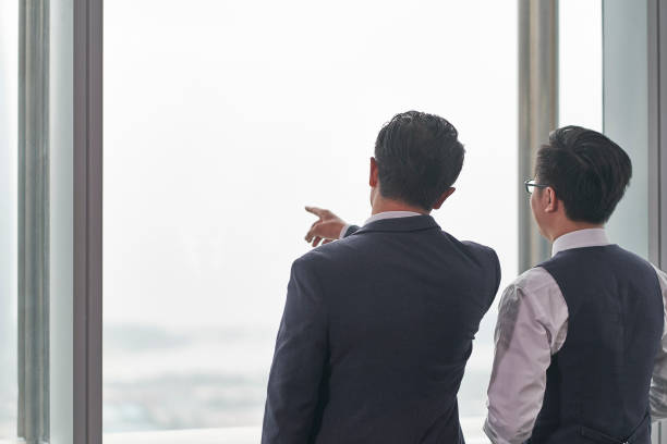 istock two asian colleagues standing in front of window talking 1296674500