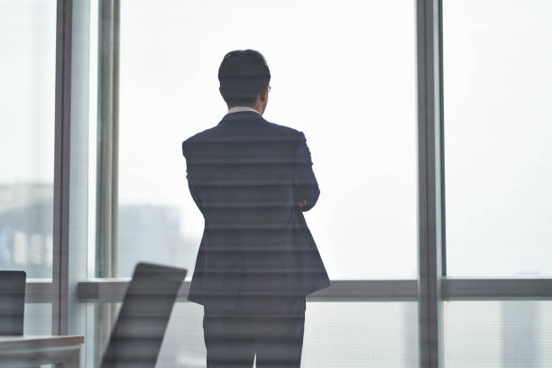 istock asian business man standing in front of office window thinking 1296674527