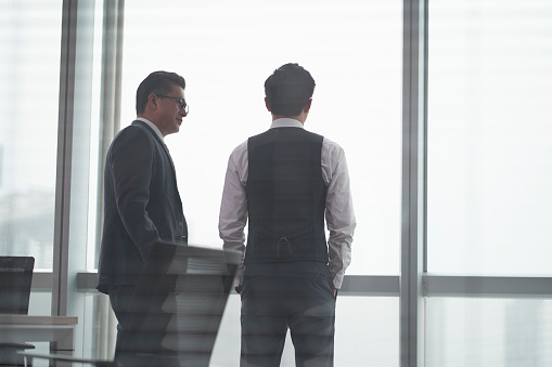 rear view of two asian business people standing in front of office window having a discussion