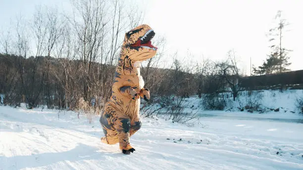 A man in a Tirex dinosaur costume walks through the forest in winter.