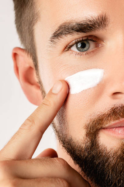 istock Young man is applying moisturizing and anti aging cream on his face 1296680530