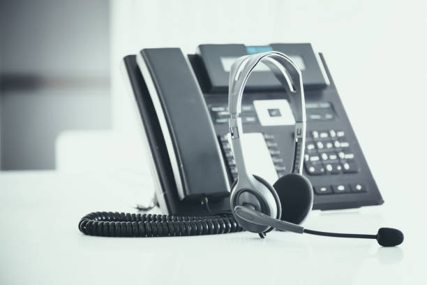 istock Communication support, call center and customer service help desk. VOIP headset on telephone keyboard. 1296681939