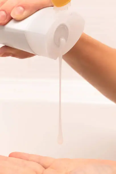 Photo of female hands pour shampoo into the palm from a bottle in a bathroom on a light background