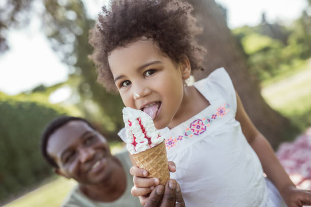 istock Dark-skinned cute kid eating ice-cream and spending time with dad 1296686343