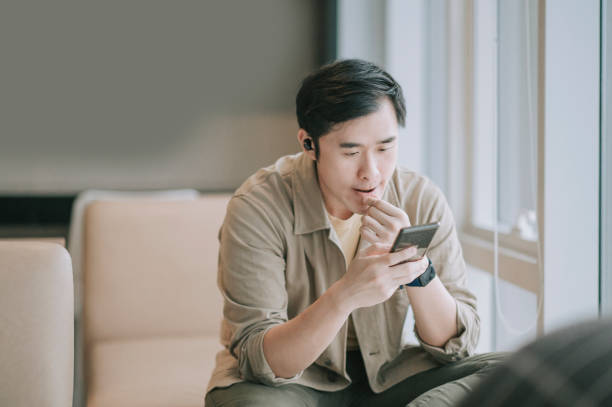 asiático hombre chino sentado en el sofá sala de estar usando el teléfono inteligente navegar por la red - mobile phone telephone bluetooth men fotografías e imágenes de stock