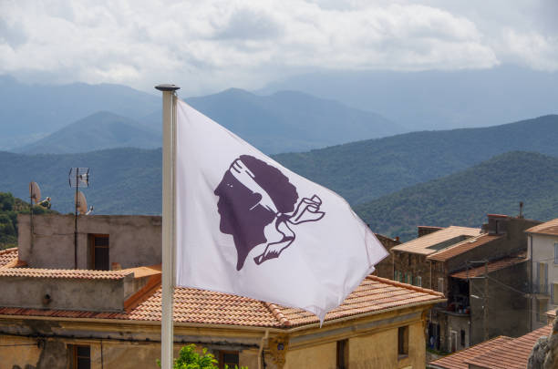 Corsican flag in front of houses and mountains in Central Corsica Corsican flag in front of houses and mountains in Central Corsica. High quality photo corsican flag stock pictures, royalty-free photos & images