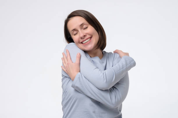 Middle age woman wearing hugging oneself happy and positive, smiling confident Middle age woman wearing hugging oneself happy and positive, smiling confident. Self love and self care hugging self stock pictures, royalty-free photos & images
