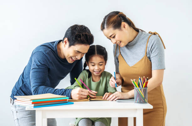 Asian young mother and father with little daughter sit at desk learning and writing in book with pencil making homework at home.Education concept. Asian young mother and father with little daughter sit at desk learning and writing in book with pencil making homework at home.Education concept. teacher classroom child education stock pictures, royalty-free photos & images