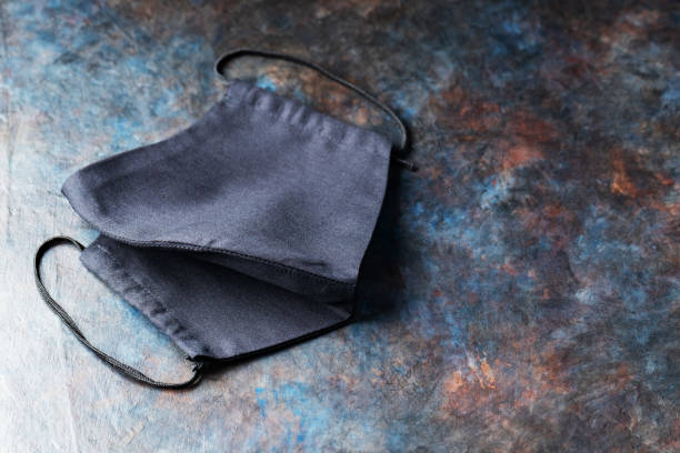 istock Handmade black protective mask on a dark background. Antivirus reusable face mask on the table. Copy space. Top view 1296703010