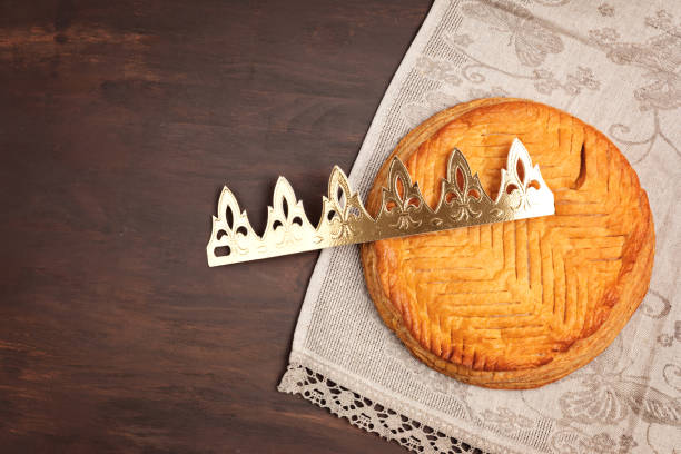 King cake or galette des rois in French. Traditional epiphany pie with golden paper crown and tiny charms King cake or galette des rois in French. Traditional epiphany pie with golden paper crown and tiny charms. Top view, flat lay galette stock pictures, royalty-free photos & images