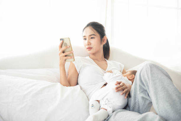 mãe da ásia segurando seu filho bebê e usar smartphone para falar com sua amiga - sucking asian ethnicity baby mother - fotografias e filmes do acervo