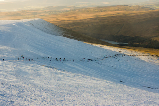 Long line of hikers above the snowline on a mountain trail (Pen-y-Fan, Wales)