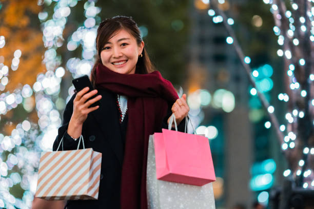 istock Woman smiling for camera while holding shopping bags and using smart phone 1296714373