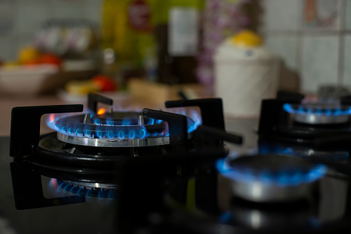 Natural gas stove. Blue flames on the black stove. Blue flames in a kitchen gas stove. Natural gas flames high resolution detail shot. Close-Up Of Lit Stove Burner Against Black Background .Natural gas fired oven, stove, heating systems. Natural energy