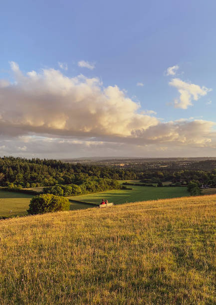 młoda para siedząca na ławce bierze w odległym widoku krajobrazu z pewley down, guildford. - surrey hill guildford cloudscape zdjęcia i obrazy z banku zdjęć