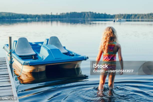 Cute Blonde Girl Walking To Pedal Boat In Lake Water On Sunset Summer Sport Water Outdoors Activity Real Authentic Happy Childhood Lifestyle View From Back Behind Stock Photo - Download Image Now