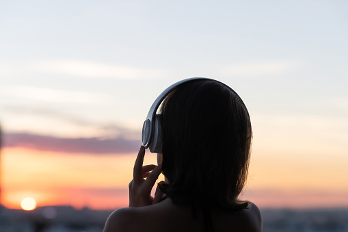 Back view silhouette of relaxed woman wearing headphones meditating listening to music on the beach at sunset