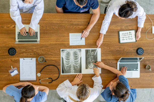 Overhead view of healthcare workers discussing x-ray image An aerial view of healthcare workers consisting of doctors and nurses in a meeting together to discuss an x-ray image. civilian stock pictures, royalty-free photos & images